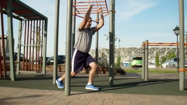 Starszy muskularny mężczyzna wykonuje ćwiczenia z elastyczną opaską na zewnątrz. Trening — Wideo stockowe