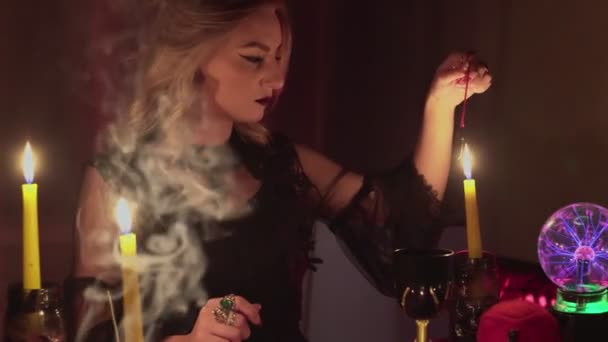 Женщина-гадалка держит волшебный маятник над свечой, а затем над фото — стоковое видео