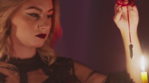 Close up of female fortune teller holding a magic pendulum over a candle — Stock Video