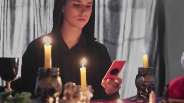 Männlicher Wahrsager betrachtet eine magische Tarokarte und bewegt sie über eine Kerze — Stockvideo
