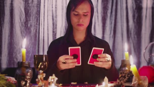 Férfi jövendőmondó okkult tarot kártyákat olvas és egy gyertya fölé rakja őket. — Stock videók