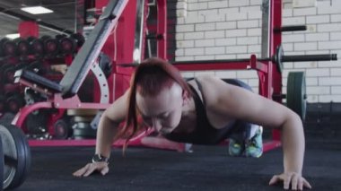 Kaslı kadın spor salonunda şınav çekiyor.