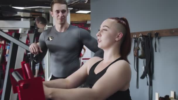 Spiervrouw traint op trainingstoestellen in de sportschool. Training met professionele trainer — Stockvideo