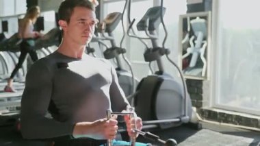 Yakışıklı sporcu spor salonunda düşük sıra makinesinde egzersiz yapıyor.