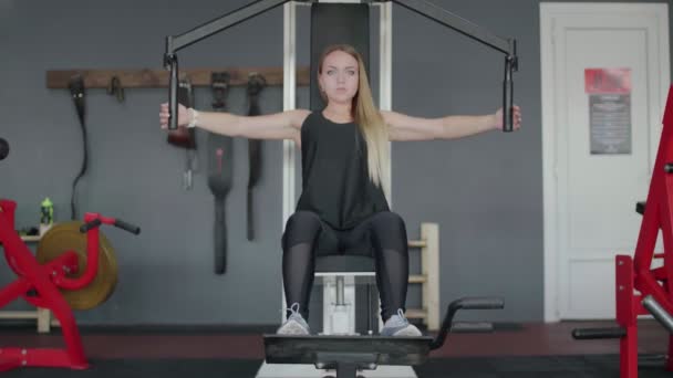 Blond vrouw traint haar borst op simulator in sportschool — Stockvideo