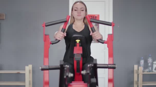 Vista frontal da mulher loira treina em aparelho de treinamento vermelho no ginásio. — Vídeo de Stock