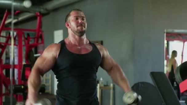 Un bodybuilder uomo attraente che esegue Side sollevare esercizio con manubri in palestra — Video Stock