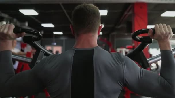 Vista posteriore di bello atletico uomo che esegue stampa sulla macchina Strength Trainer in palestra — Video Stock