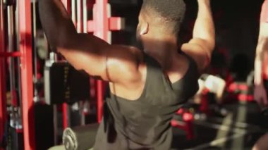 Kablosuz kulaklıklı Afrikalı Amerikalı vücut geliştirici spor salonunda Lat-down yapıyor.