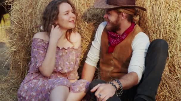 Een jong stel zit op hooi op de boerderij. Gelukkig lachende cowboy en vrouw brengen tijd samen door — Stockvideo