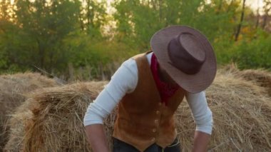 Çiftliğinde samanların yanında poz veren yakışıklı kovboy.