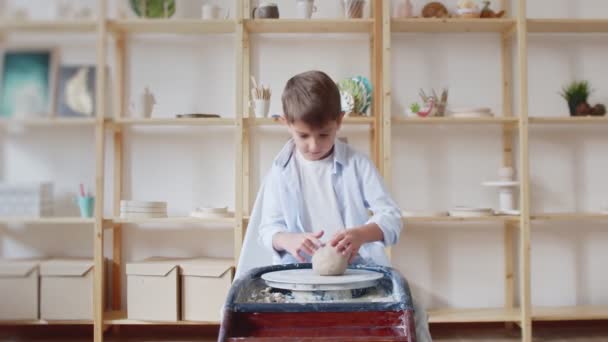 Niño intenta trabajar con rueda de cerámica y barro haciendo loza. — Vídeos de Stock