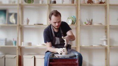 Erkek çömlekçi masadaki kil parçasını şekillendiriyor. Adam seramik bir şey yapıyor. Sanat stüdyosunda çömlekçilik, el yapımı ve yaratıcı beceriler..