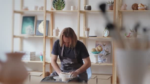Man hantverkare sitter på stol och hantverk lerkärl på hjul under arbete i rymliga professionella keramik — Stockvideo