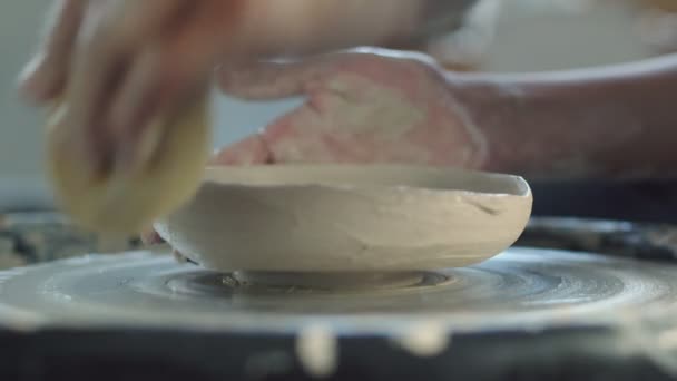 Вид сбоку женщины гончара использует губку, чтобы сделать керамический горшок на крученом гончарном круге. — стоковое видео