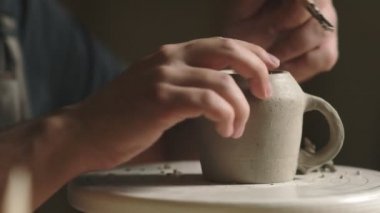 Çömlekçiyi çömlekçi stüdyosunda seramik kilden bardak yapmak için araç kullanarak kapat