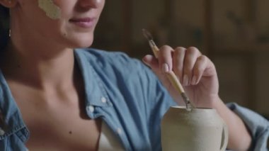 Çömlekçi kadın çömlekçiyi çömlekçi stüdyosunda seramik kil yapmak için araçlar kullanarak kapatın.