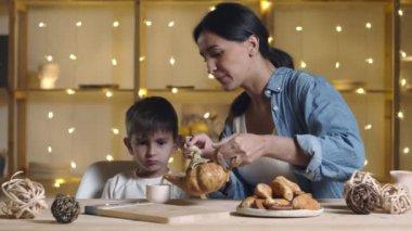 Anne ve oğul çay içip çörek ve kruvasan yiyorlar.