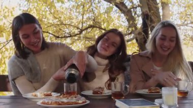 Omuzlarında battaniyeyle terasta rahatlayan üç mutlu genç kadın.