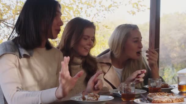 Χαλαρωμένες νεαρές γυναίκες με μια κουβέρτα στους ώμους να κάθονται στη βεράντα, πίνοντας τσάι και τρώγοντας κέικ. — Αρχείο Βίντεο