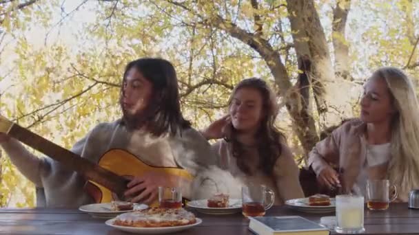 Três jovens mulheres felizes com um cobertor em seus ombros relaxa no terraço juntos. Mulher toca guitarra — Vídeo de Stock