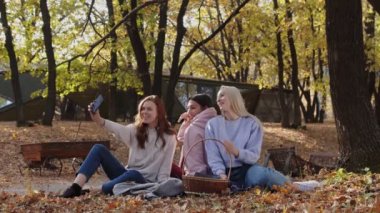 Mutlu kadın arkadaşlar sonbahar ormanında telefonda selfie çeker.