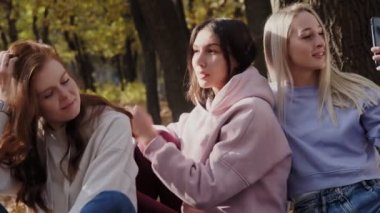 Mutlu kadın arkadaşlar sonbahar ormanında dinlenir. Kadın telefonunda video kaydı yapıyor.