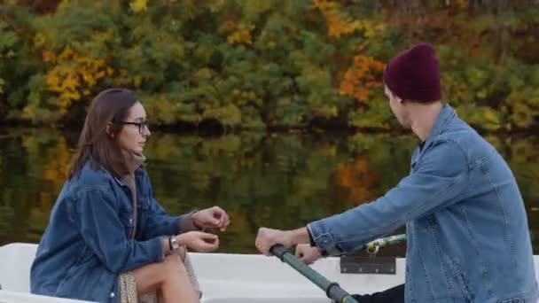 Pohledný chlap a krásná dívka plavat v lodi na jezeře v pohádkovém podzimním lese — Stock video