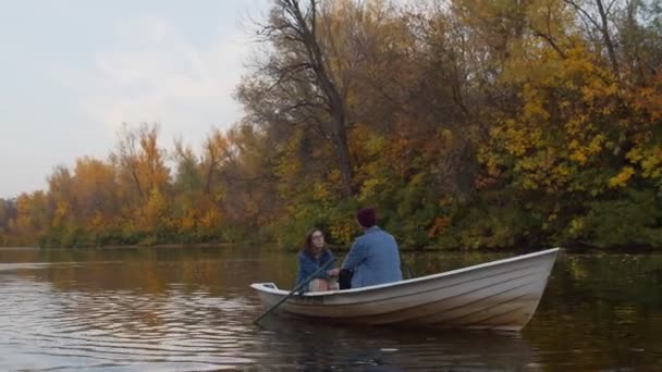 Un beau mec et une belle fille sont assis dans un bateau sur un lac dans une forêt d'automne de fées — Video