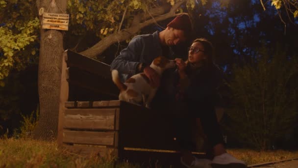Romantisk ungt par med runkende terrier sitter på benken i parken. – stockvideo