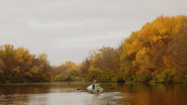 İki güzel kadın, sonbahar ormanlarında bir gölde bir teknede oturuyor.
