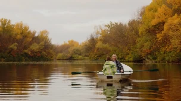 Две красивые женщины сидят в лодке на озере в волшебном осеннем лесу — стоковое видео