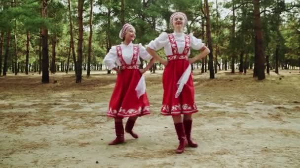 Две молодые и красивые женщины танцуют русские традиционные танцы в летнем лесу — стоковое видео