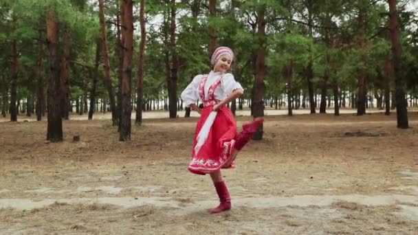 Молода і красива жінка, одягнена в російський традиційний костюм, танцюють російські танці в лісах. — стокове відео