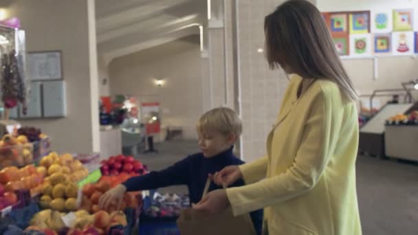 Мальчик с матерью на рынке. Мальчик кладет мандарины в бумажный пакет — стоковое видео