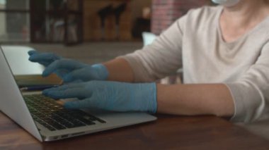 Koruyucu maskeli ve eldivenli bir bayan kafede defter üzerinde çalışıyor.