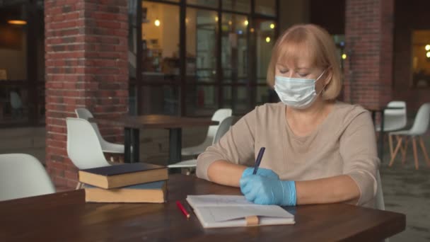 Escritora de libros con máscara protectora y guantes trabaja en cafetería — Vídeos de Stock