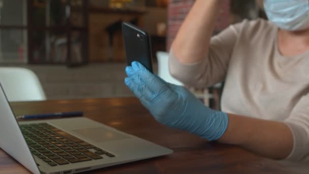 Närbild av dam med skyddsmask och handskar använder telefon på café — Stockvideo