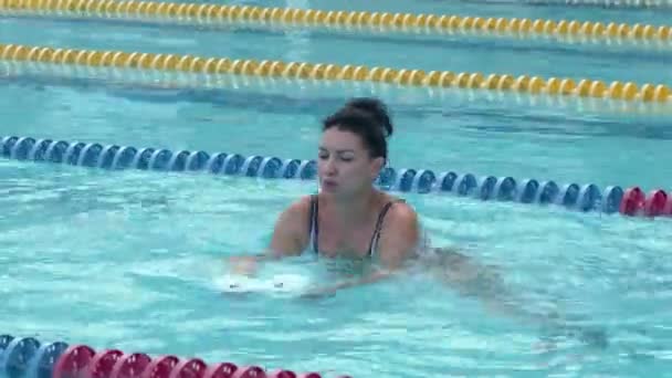 Женщина тренирует аква-гимнастику с гантелями из пенопласта в бассейне. — стоковое видео