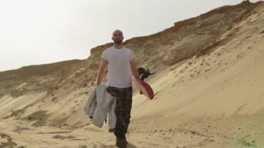 Yakışıklı kaslı adam çölde ya da taş ocağında kumla yürüyor.