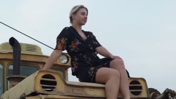 Barfüßige blonde Frau sitzt auf altem Traktor — Stockvideo