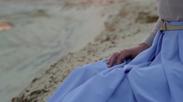 Close-up van jonge brunette in blauwe rok zit op de top van zand heuvel met zonsondergang op de achtergrond — Stockvideo