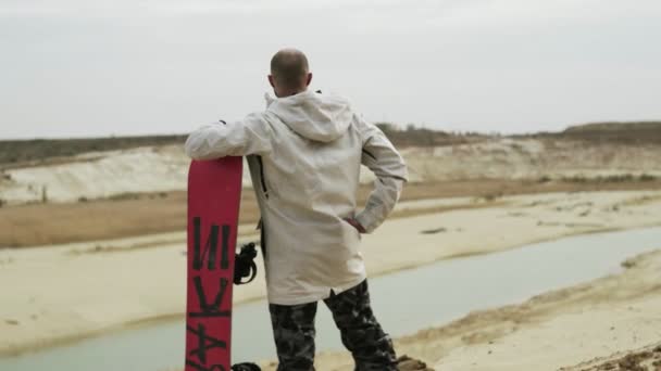 Vue arrière du bel homme chauve posant avec un panneau de sable dans le désert ou la carrière de sable — Video