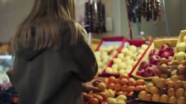 Arkaya bakan genç bir kadın marketteki raflardan erik seçiyor.