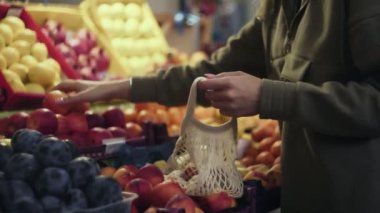 Genç bir kadın markette kırmızı aperatifi ip torbasına koyuyor.