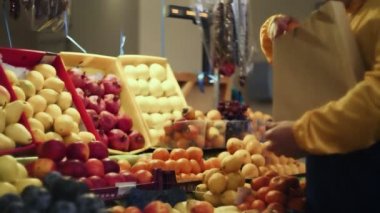 Bir adam taze bir mandalina seçer, onları bir kese kağıdına koyar ve onu markette satıcıya verir.