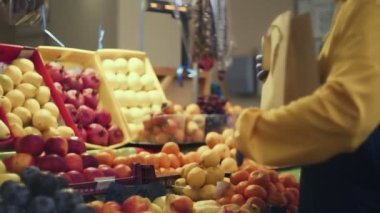 Bir adam taze bir mandalina seçer ve onları markette bir kese kağıdına koyar.