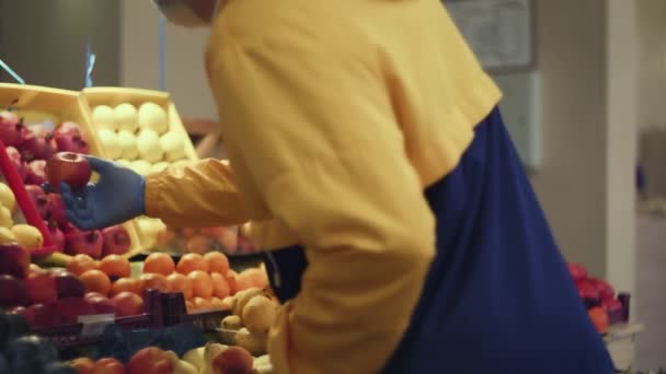 Hombre joven huele y elige manzanas en los estantes de la tienda en el mercado — Vídeo de stock