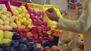 Sarı montlu kadının arka görünüşü markette kırmızı elmaları ipe takıyor.