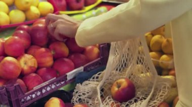 Sarı montlu kadının arka görünüşü markette kırmızı elmaları ipe takıyor.